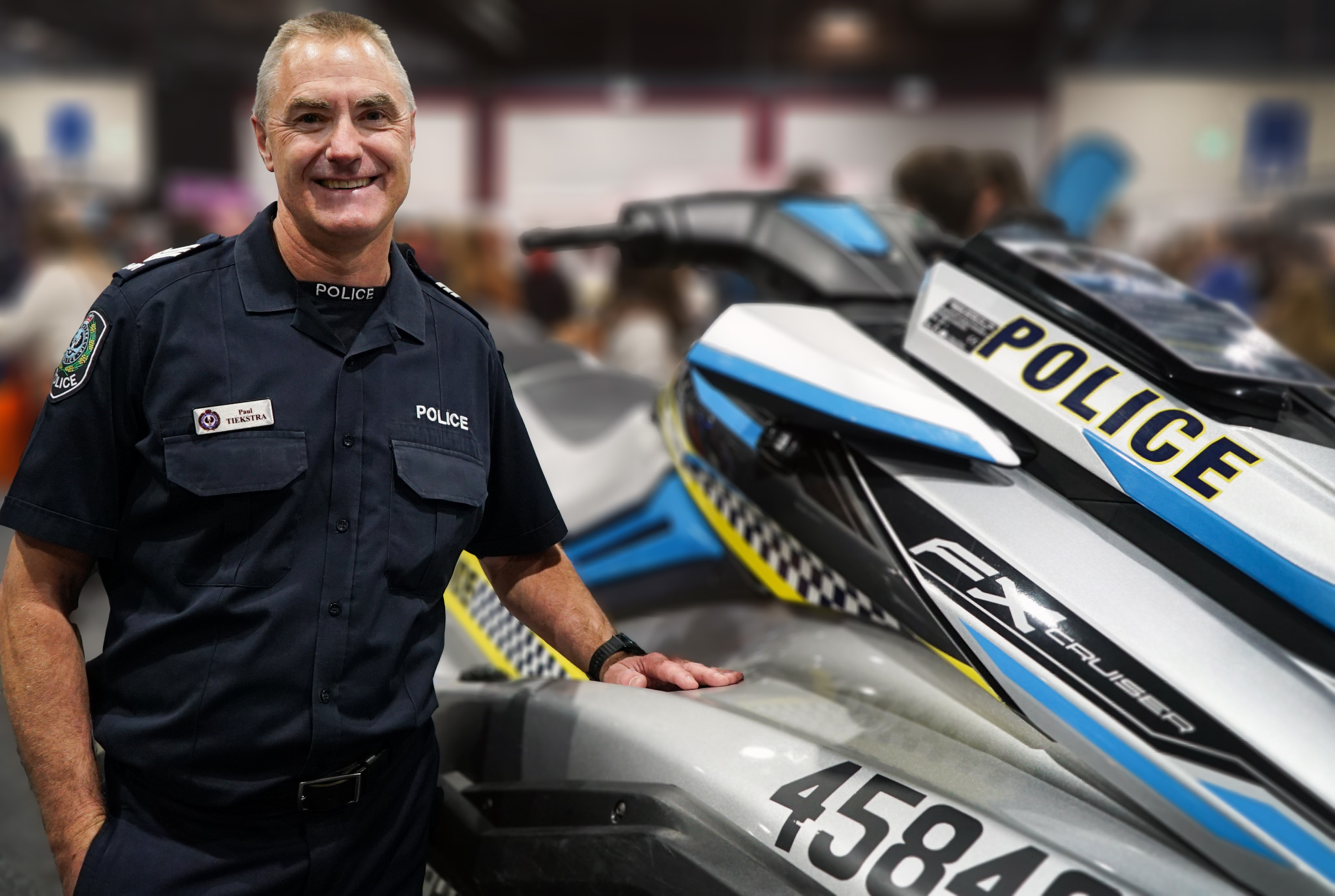 A smiling male police officer leaning on a police jet ski